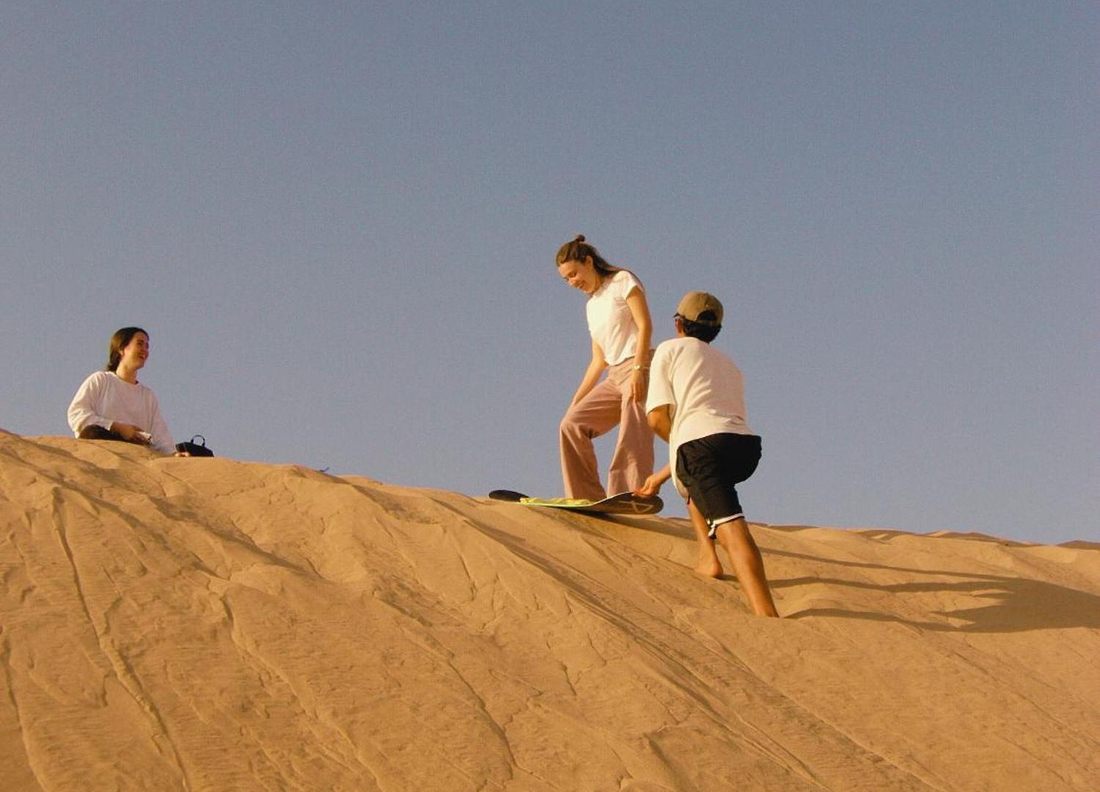 Guest sandboarding down a dune on a day trip from the house
