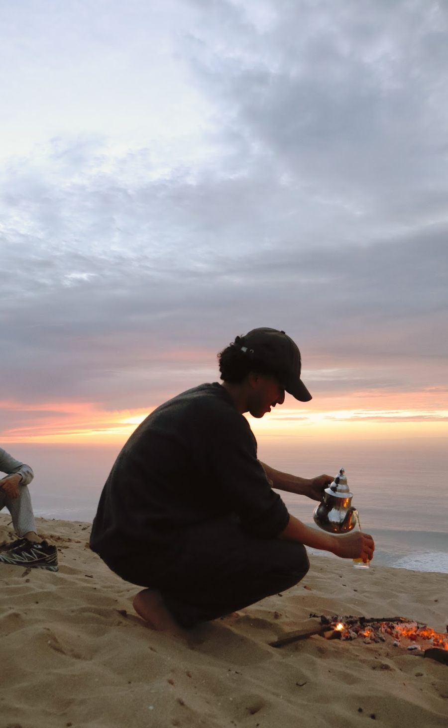 Tea brewed over a small fire on the beach at sunset